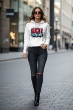 Woman wearing a white hoodie with graphic design and text, black jeans, and black boots on a city street.