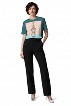 A model wearing a short-sleeve color-blocked top with a graphic print on the front, paired with black trousers and silver heels, against a plain white background.