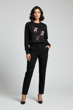 Woman wearing a black sweater with floral patterns and black pants on a light gray background