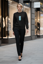 Woman wearing a black sweater with a graphic design and black pants walking on a street.