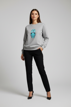 Woman wearing a gray sweatshirt with an owl design and black pants on a light gray background