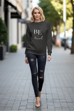 Woman wearing a black sweatshirt with 'BE' text on a city street.