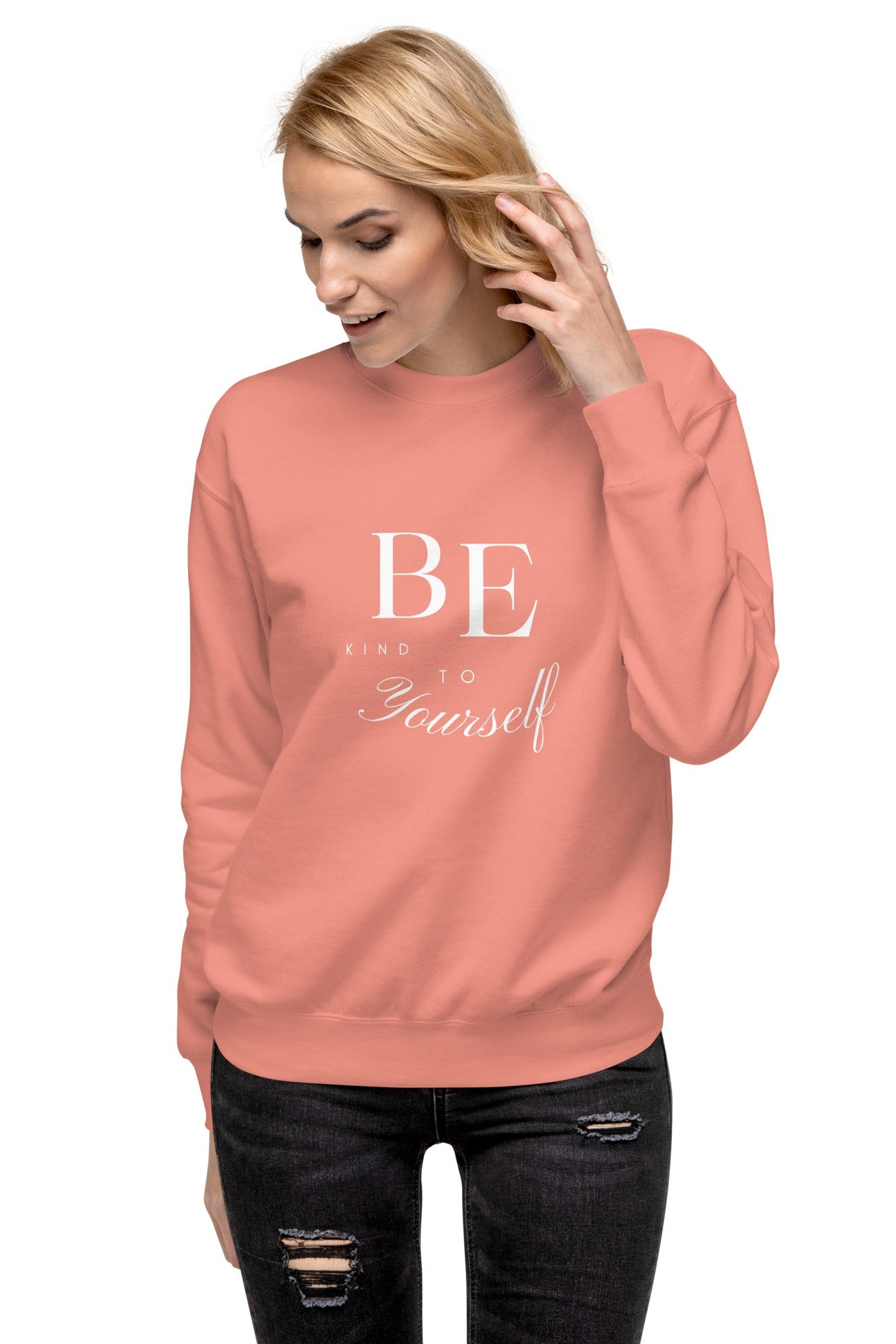 A woman wearing a pink graphic sweatshirt with the text 'BE YOURSELF' on it.