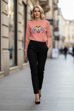 Woman wearing a pink sweatshirt with a graphic design and black pants walking on a city street.