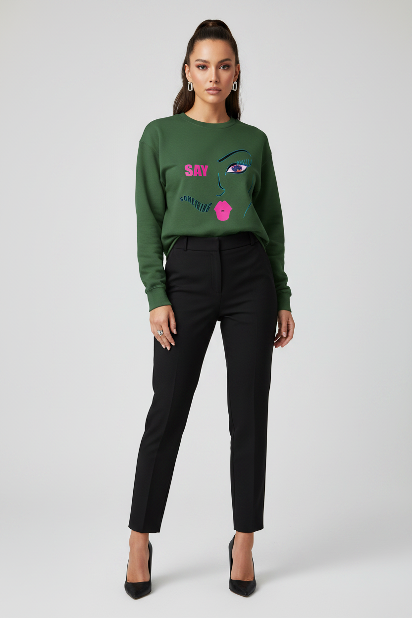 Woman wearing a green sweater with a face design and black pants on a white background