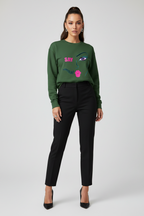 Woman wearing a green sweater with a face design and black pants on a white background