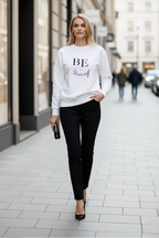 Woman wearing a white sweatshirt with text and black pants on a city street.