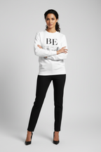 Woman wearing a white sweater with text and black pants on a gray background