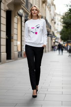 Woman wearing a white sweatshirt with a face design on a city street.