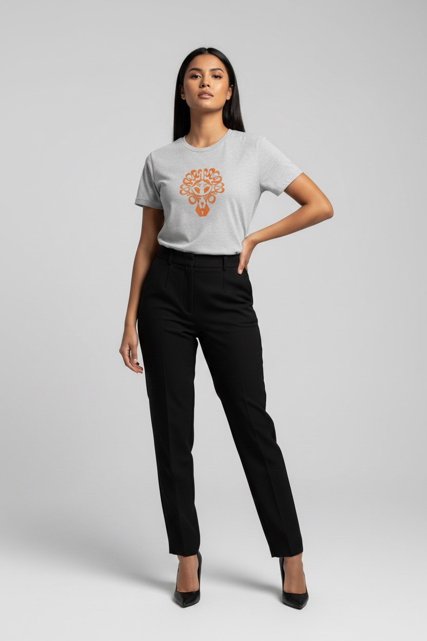 A woman modeling a light gray short-sleeve t-shirt with an orange mandala graphic on the chest, paired with black trousers and black heels, against a light gray studio background.