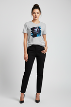 A woman modeling a light gray short-sleeve t-shirt with a blue and black graphic print on the front, paired with black pants and black heels, against a light gray studio background.