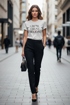 Woman walking down a city street wearing a white t-shirt with text and black pants.
