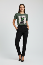 A woman modeling a dark green graphic t-shirt with a black and white French Bulldog print, paired with black trousers and black heels, against a light gray studio background.