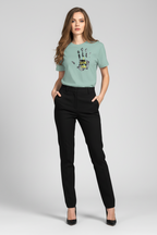 Woman wearing a light green t-shirt with a graphic design and black pants on a white background