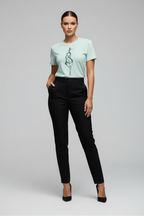 Woman wearing a light green t-shirt with a graphic design and black pants on a gray background