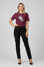 A woman modeling a short-sleeve crewneck t-shirt in deep burgundy with a colorful graphic print on the front, paired with black trousers and black heels, against a light gray studio background.