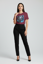 A woman modeling a short-sleeve crewneck t-shirt in maroon with a large graphic print of a woman's face in blue and black tones, paired with black trousers and black heels, against a light gray studio background.
