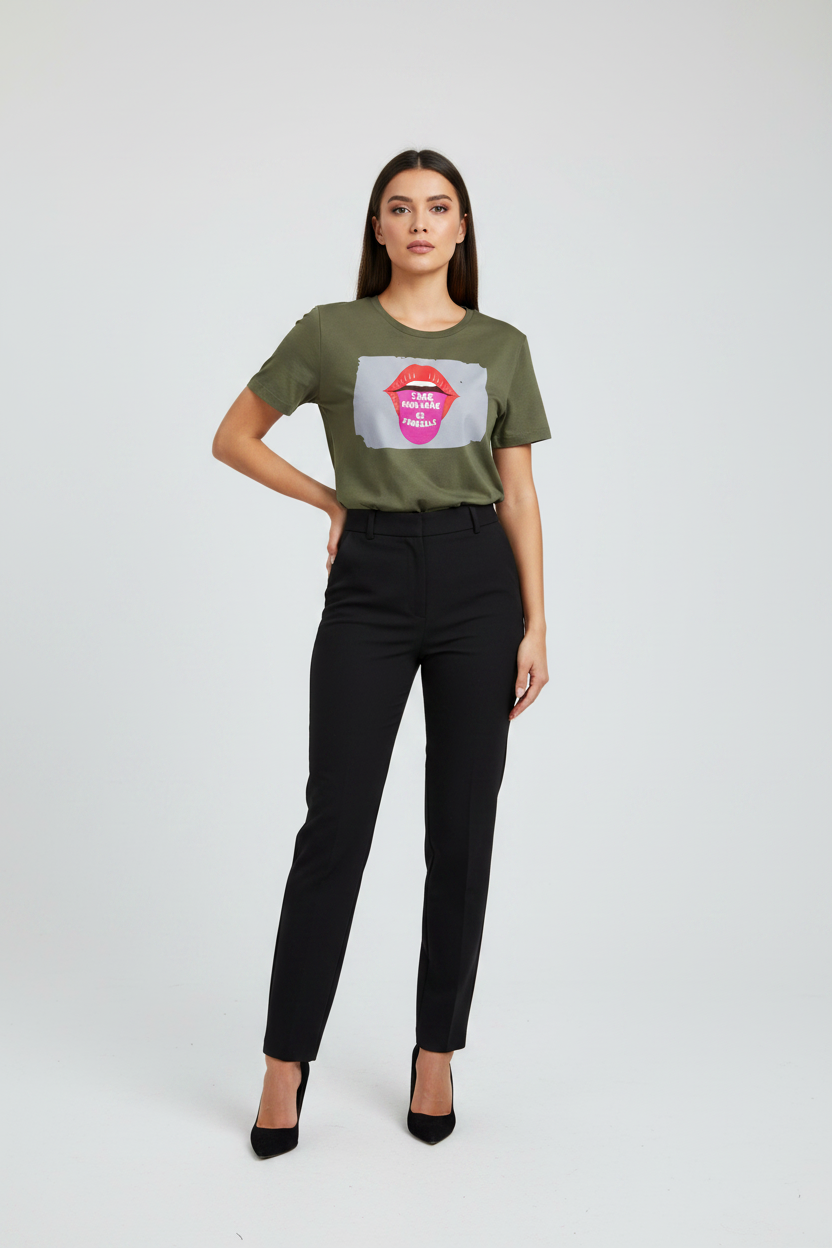 A woman modeling a short-sleeve olive green graphic t-shirt with a pink lips print and black high-waisted trousers, standing against a light gray studio background.