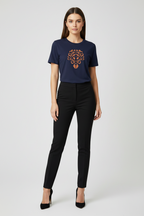 A woman modeling a navy blue short-sleeve t-shirt with a brown and orange graphic print on the chest, paired with black pants and black heels, against a light gray studio background.
