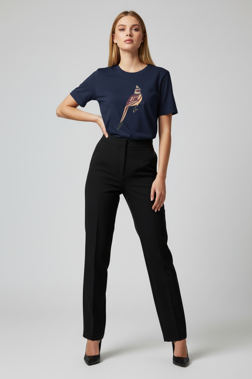 A woman modeling a navy blue short-sleeve t-shirt with a colorful bird graphic on the chest, paired with black trousers and black heels, against a light gray studio background.