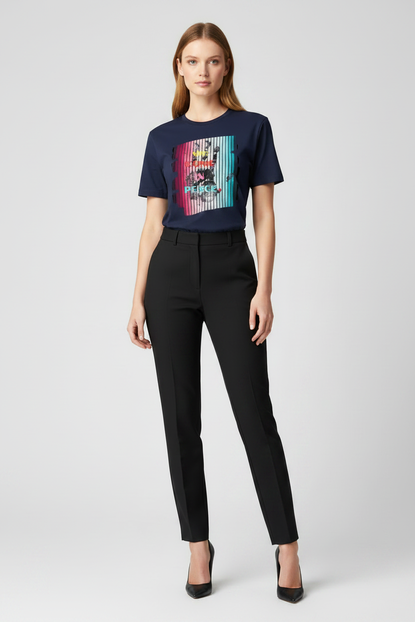 Woman wearing a navy t-shirt with a colorful graphic and black pants on a white background