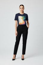 Woman wearing a navy t-shirt with a colorful graphic and black pants on a white background