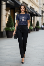 Woman walking on a city street wearing a navy blue t-shirt with text and black pants.