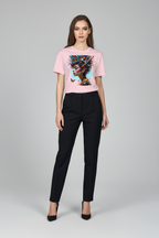 A woman modeling a light pink short-sleeve t-shirt with a colorful graphic print of a woman's profile, paired with black trousers and black heels, against a light gray studio background.