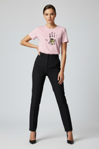 Woman wearing a pink t-shirt with a graphic design and black pants on a light gray background