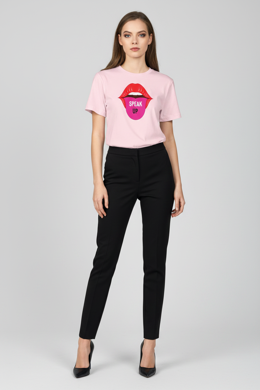 A woman modeling a light pink short-sleeve t-shirt with a graphic of red lips and a pink tongue showing the words 'OPEN UP' in black, paired with black pants and black heels, against a light gray studio background.