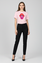 A woman modeling a light pink short-sleeve t-shirt with a graphic of red lips and a pink tongue showing the words 'OPEN UP' in black, paired with black pants and black heels, against a light gray studio background.