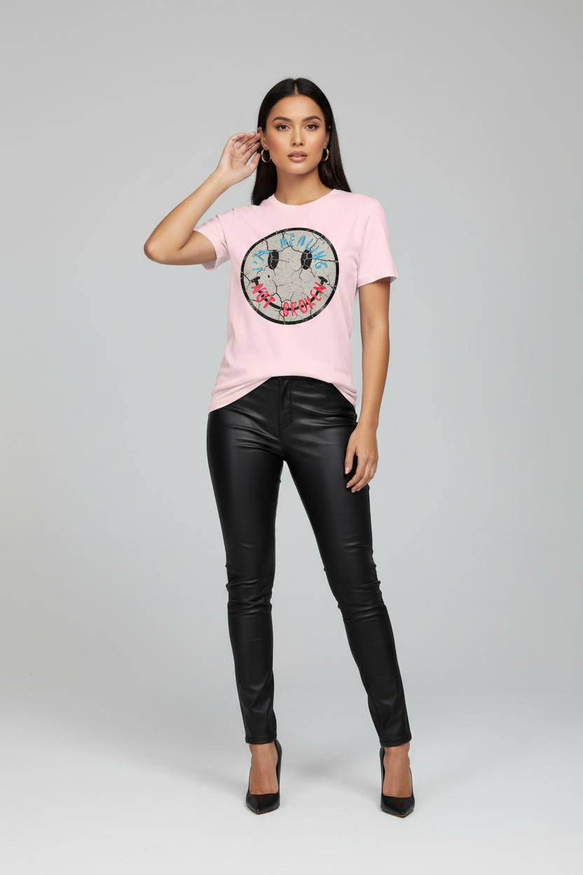 Woman wearing a pink t-shirt with a smiley face design and black leather pants on a gray background