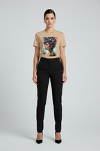 A model stands against a light gray studio background wearing a beige graphic T-shirt with a colorful portrait print, black trousers, and black heels.
