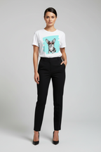 A woman modeling a white short-sleeve crewneck t-shirt with a graphic print of a Chihuahua dog on a light blue background, paired with black trousers and black heels, against a light gray studio background.