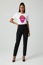 A woman modeling a white graphic T-shirt with a pink and red lips design and the word 'SPEAK UP' on the front, paired with black pants and black heels, against a light gray studio background.