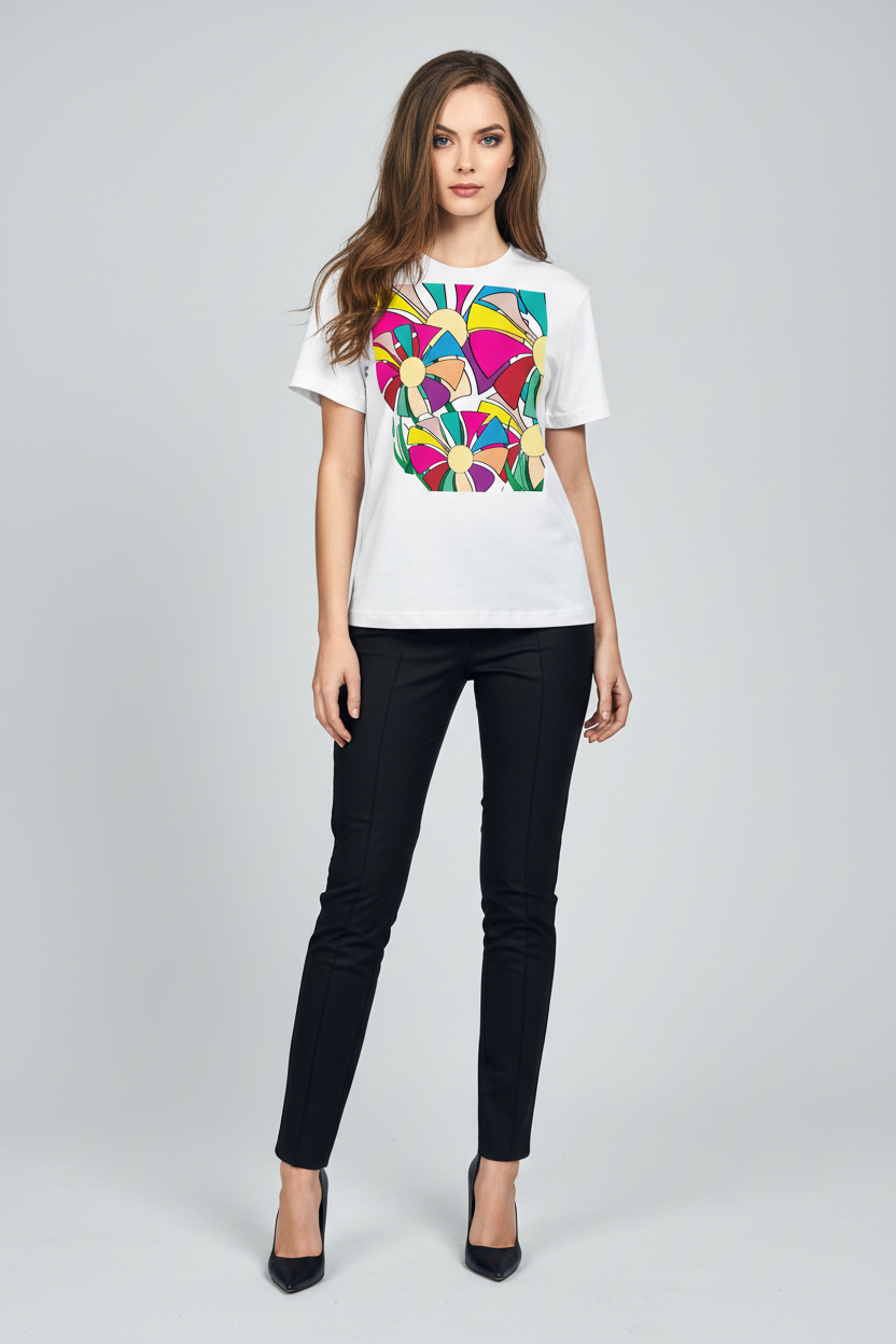 A woman modeling a white short-sleeve t-shirt with a colorful geometric heart graphic on the front, paired with black pants and black heels, against a light gray studio background.