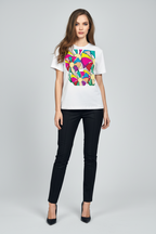 A woman modeling a white short-sleeve t-shirt with a colorful geometric heart graphic on the front, paired with black pants and black heels, against a light gray studio background.