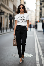 Woman walking on a city street wearing a white t-shirt with text and black pants.