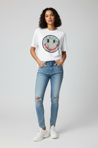 Woman wearing a white t-shirt with a colorful smiley face design and blue jeans on a light gray background
