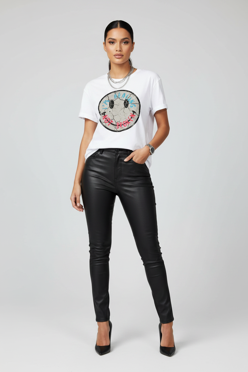 Woman wearing a white t-shirt with a smiley face design and black leather pants on a white background